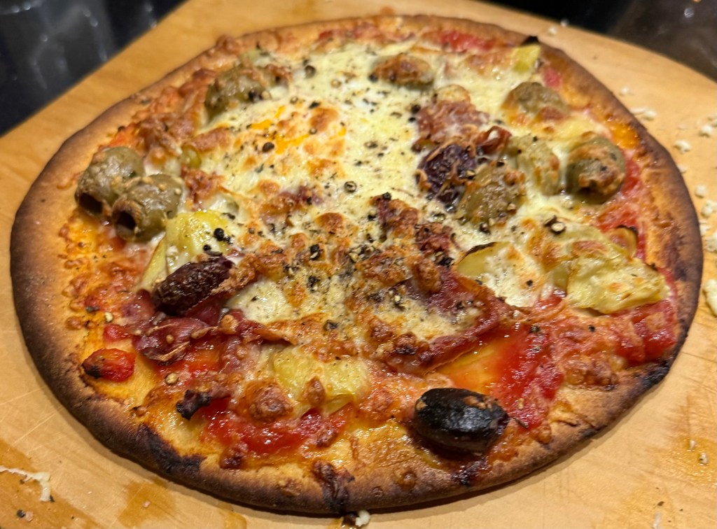 Pizza with egg, prosciutto, artichokes, olives, mozzarella, tomato sauce, and basil